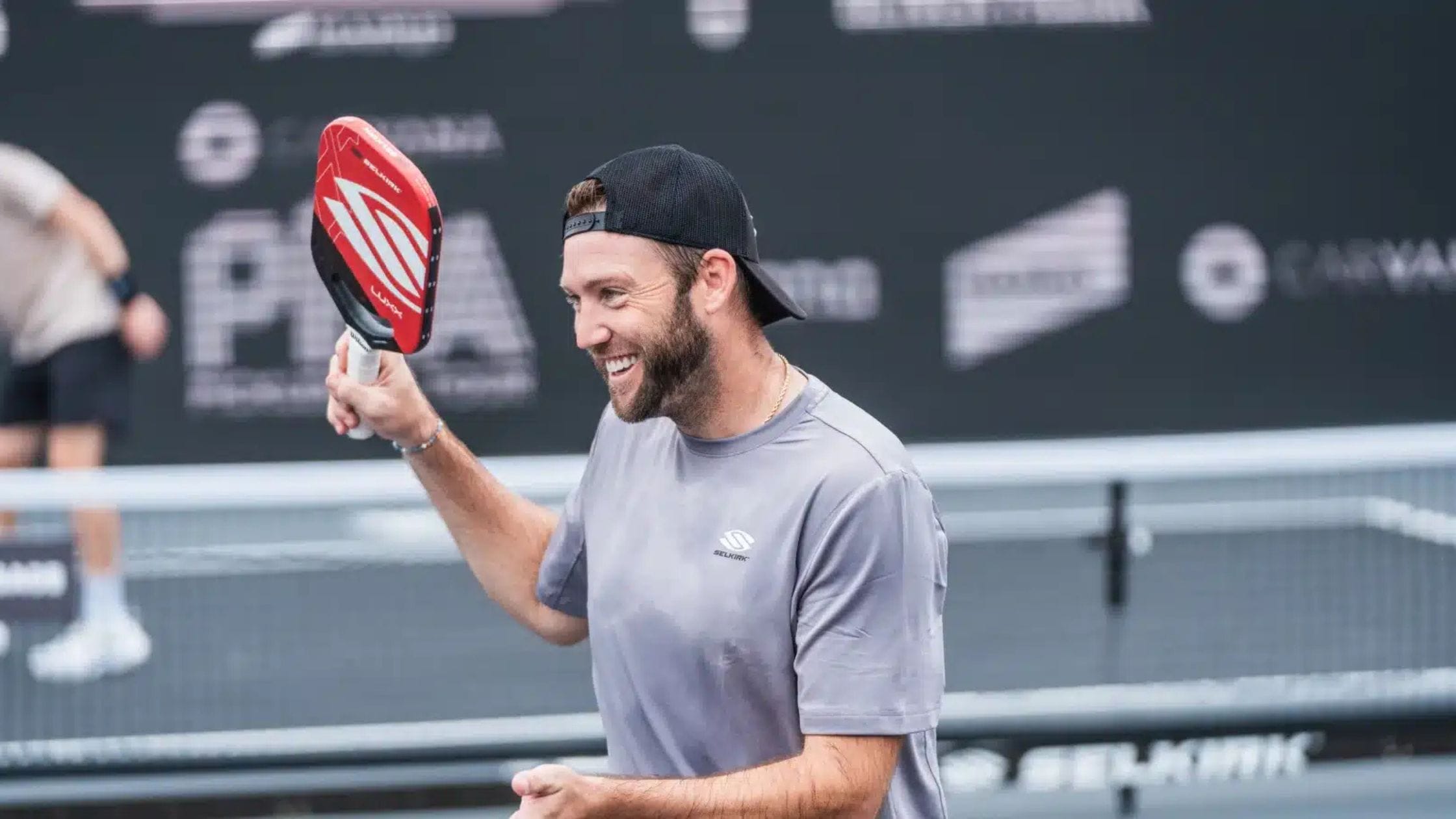 A smiling pickleball player holding a red Selkirk paddle on the court, showcasing one of the best pickleball paddles of 2025.