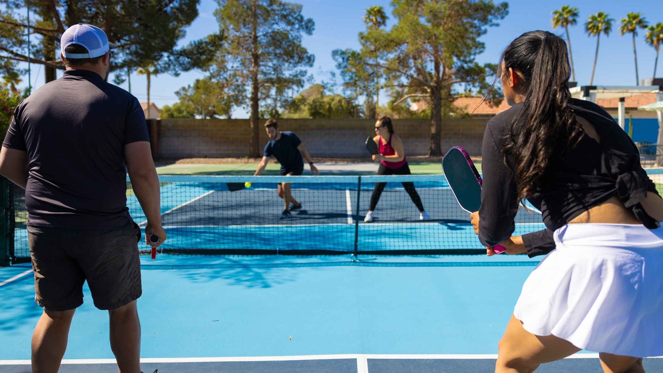 Two teams playing a competitive pickleball tournament on an outdoor court under a sunny sky.