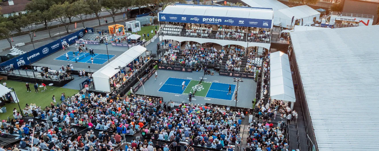 A large crowd gathers around professional pickleball courts at a major pickleball event, showcasing an exciting atmosphere and competitive play.