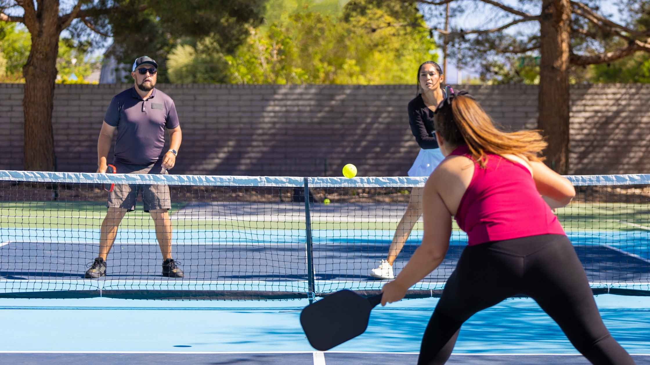 A group of beginner pickleball players engaged in a doubles match on an outdoor court, demonstrating essential pickleball techniques and strategies.