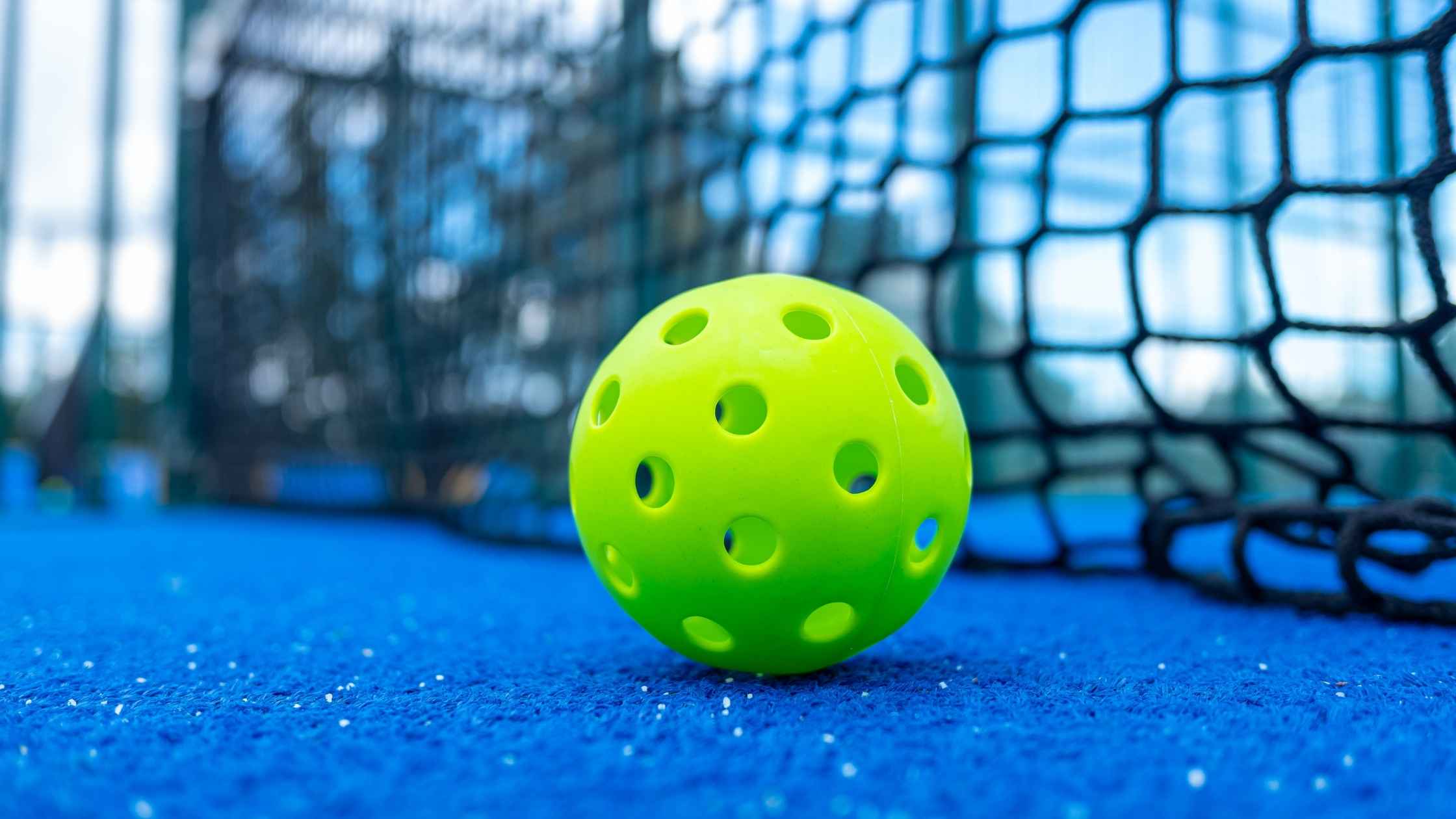 A bright green pickleball resting on a blue court near the net in Santa Cruz.