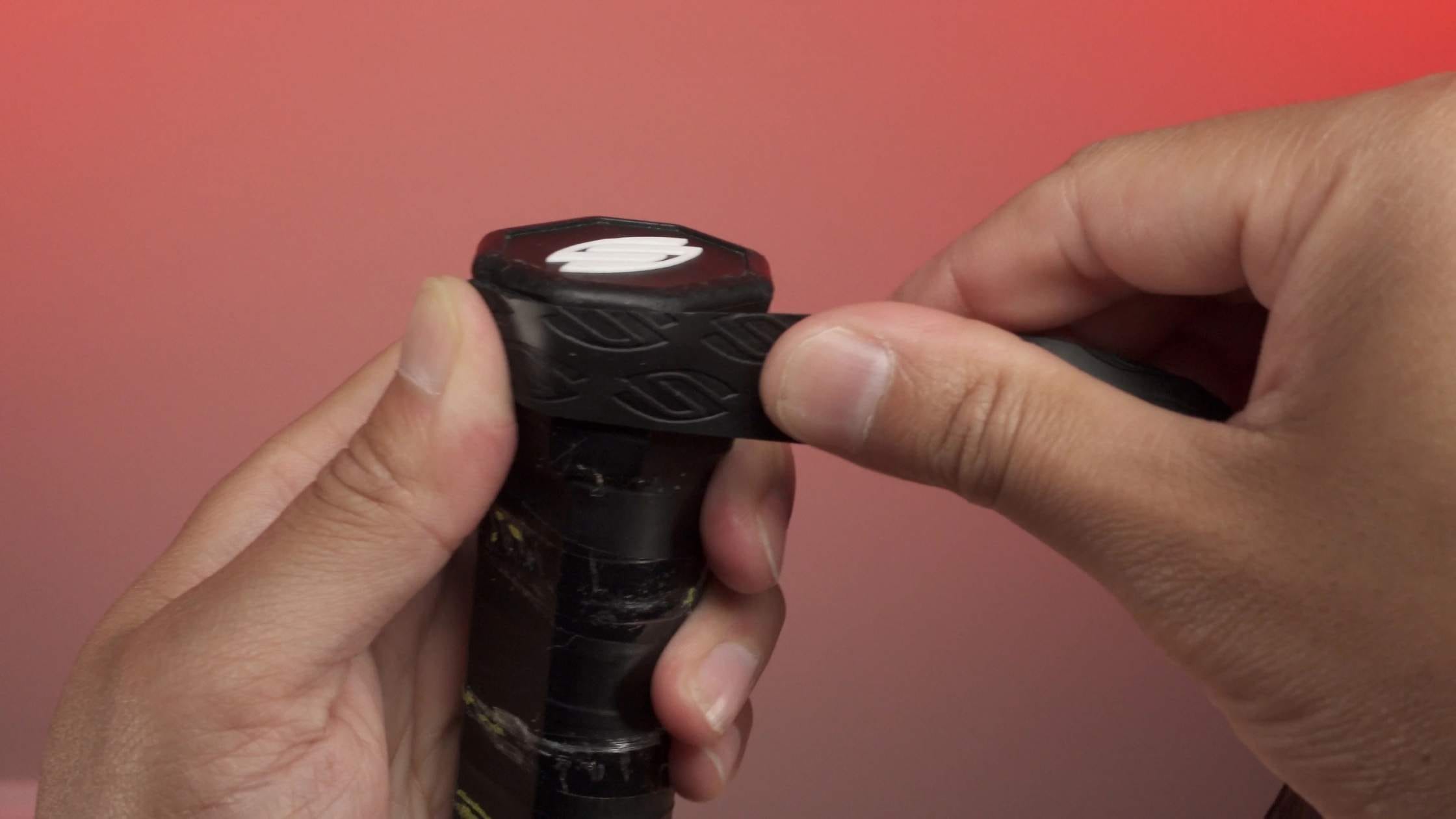 Close-up of hands regripping a pickleball paddle with a black grip against a red background.