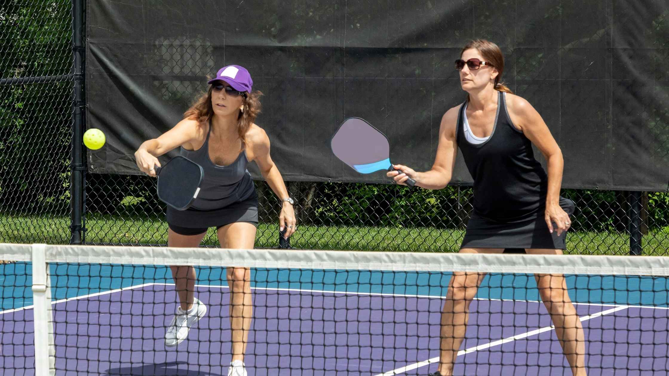 Two women playing a doubles round robin pickleball match on an outdoor court, focused on returning the ball with their paddles.