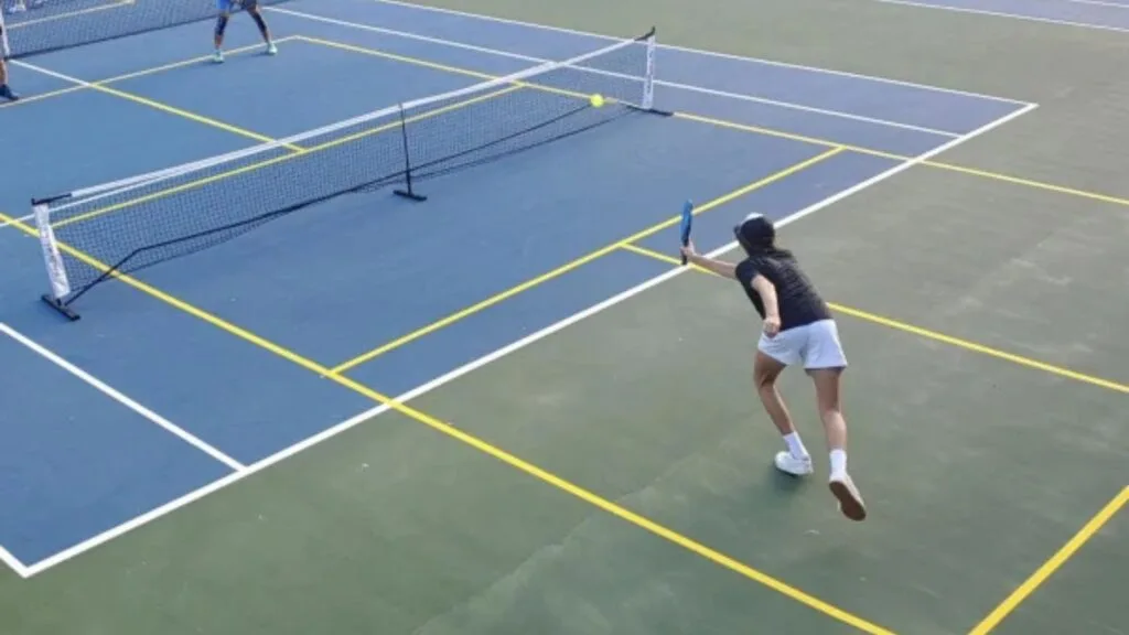 Two players actively playing pickleball on a tennis court with bright yellow lines marking the pickleball boundaries.
