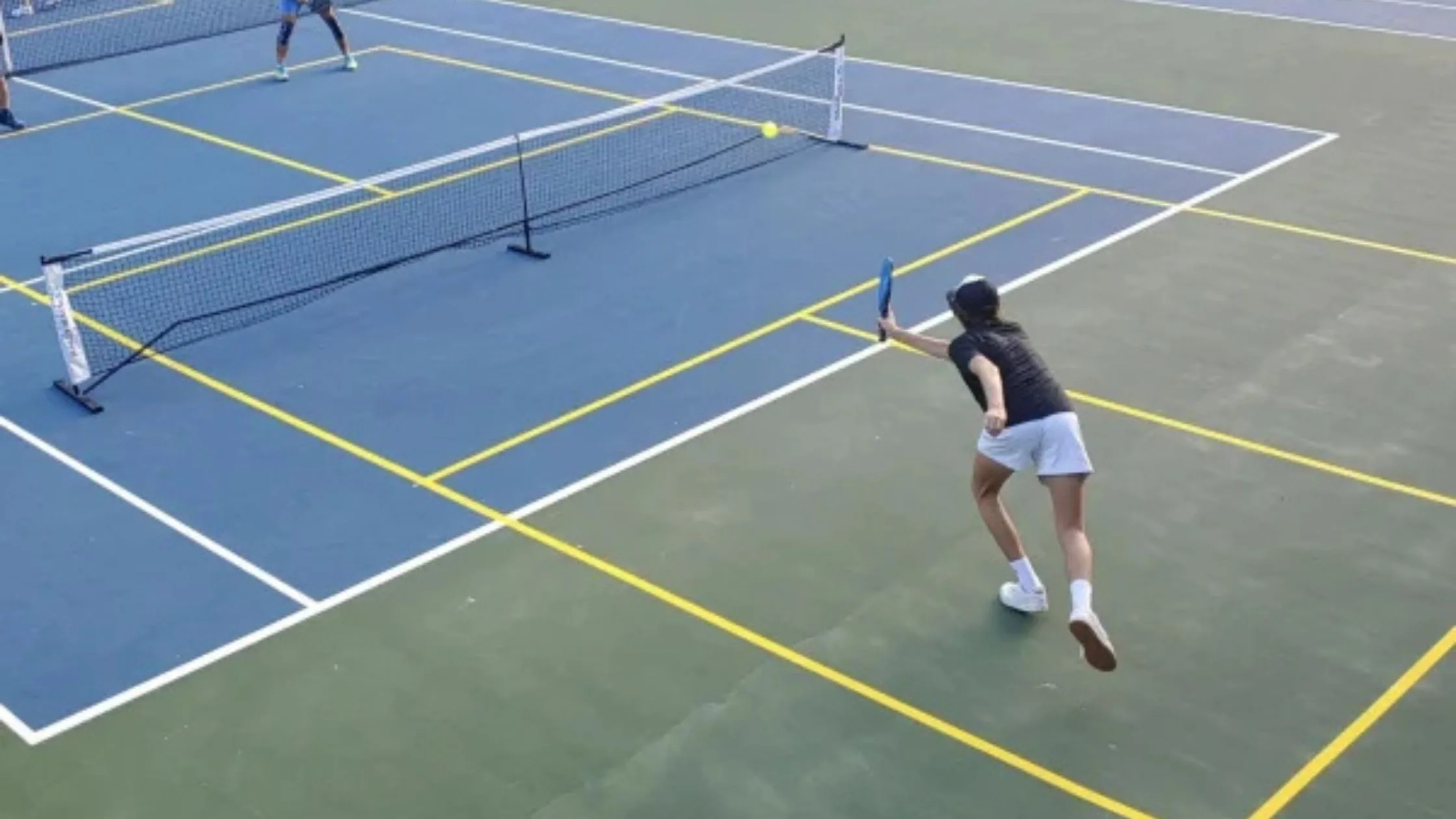 Two players actively playing pickleball on a tennis court with bright yellow lines marking the pickleball boundaries.